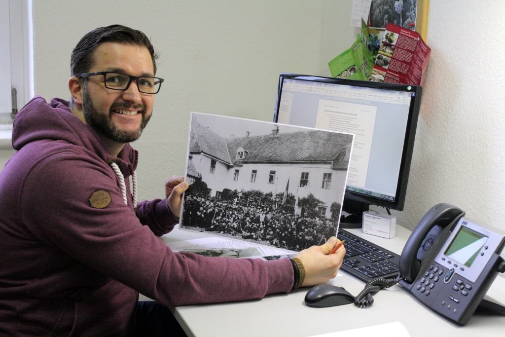 Volontär Stephan Pieper mit einem historischen Foto des Alten Kreishauses. Es zeigt eine Schützengesellschaft vor dem Kanzleiflügel des heutigen Museums. © Bachmann-Museum Bremervörde