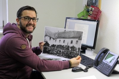 Volontär Stephan Pieper mit einem historischen Foto des Alten Kreishauses. Es zeigt eine Schützengesellschaft vor dem Kanzleiflügel des heutigen Museums. © Bachmann-Museum Bremervörde