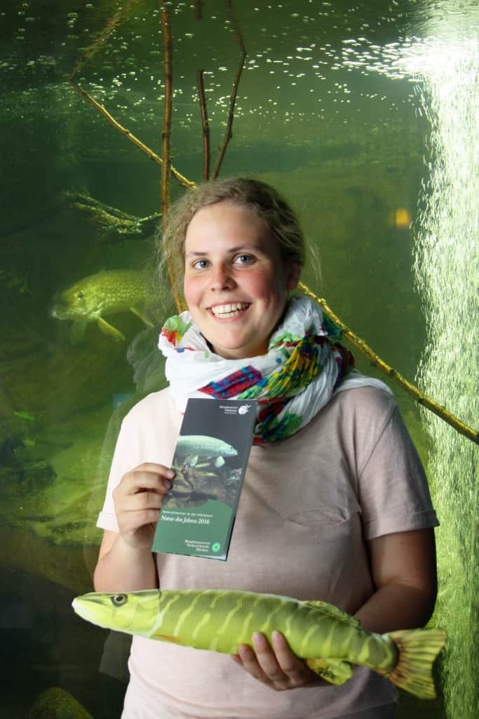 Claire Löchner mit ihrem Faltblatt zur Natur des Jahres vor dem Hechtbecken im Biosphaerium Elbtalaue, Foto Biosphaerium Elbtalaue
